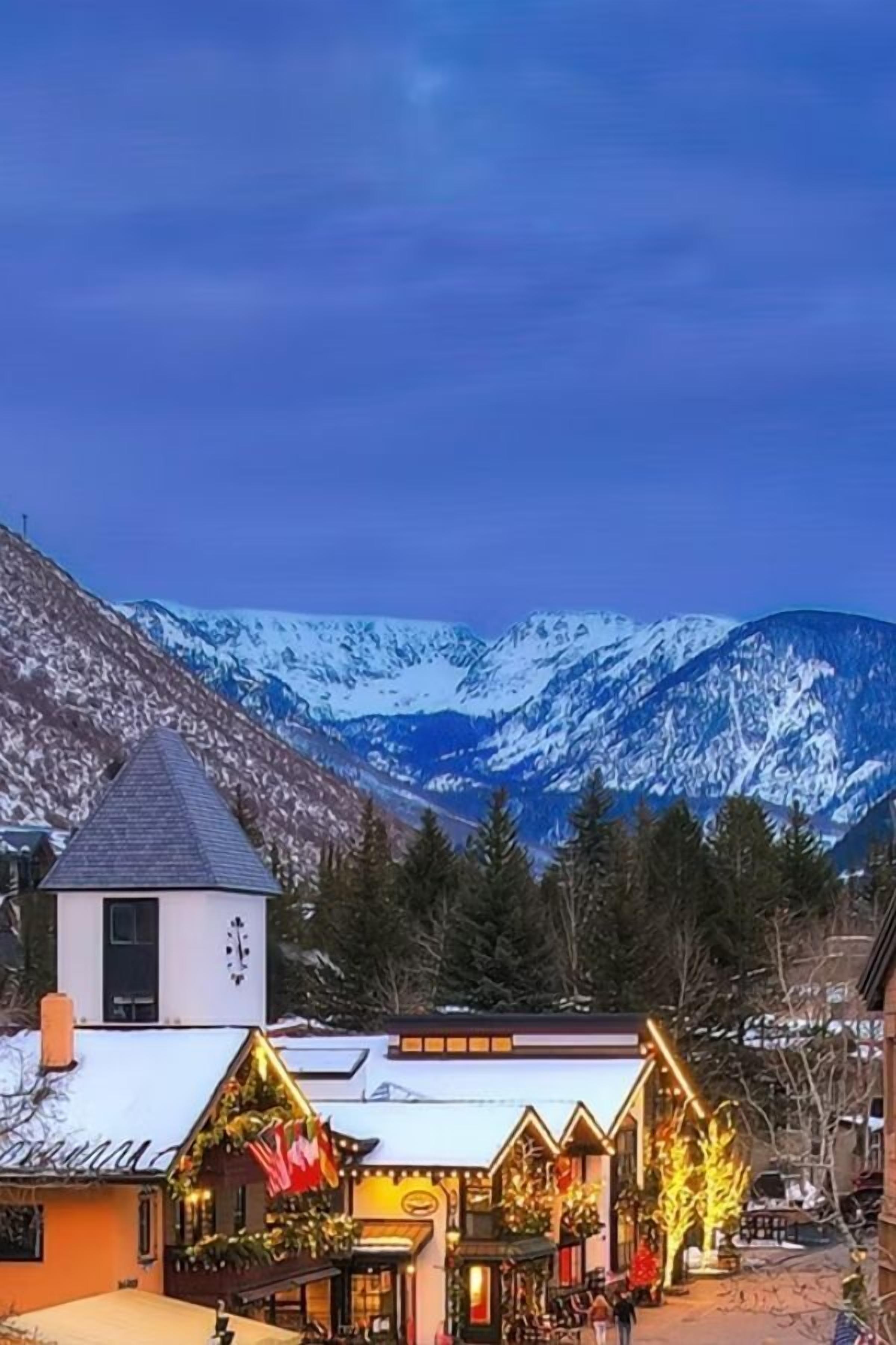 Un edificio con techo nevado y un campanario, rodeado de montañas cubiertas de nieve.