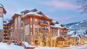 A large, multi-story lodge with a stone facade, multiple balconies, and a snow-covered landscape.