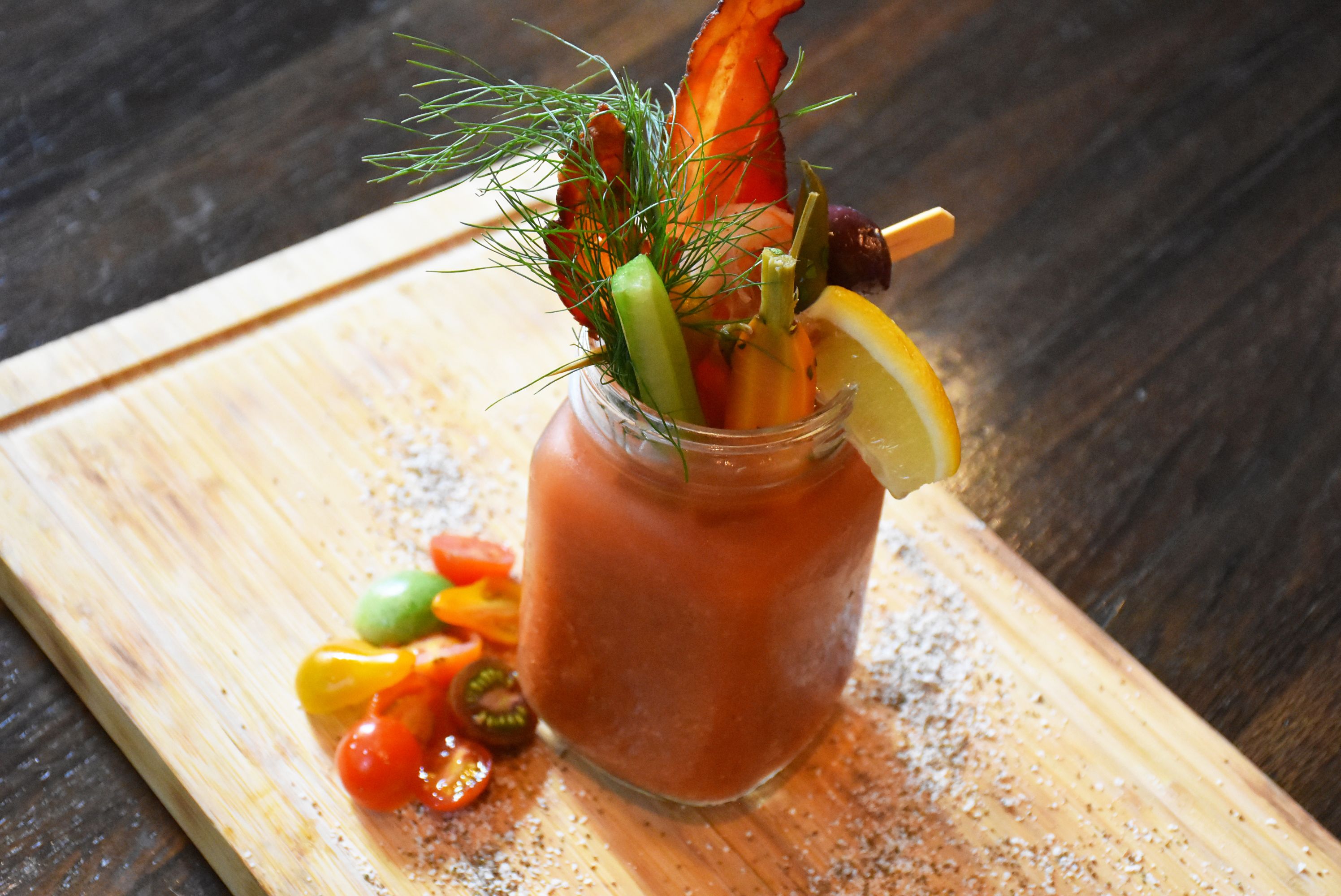 A glass of Bloody Mary with garnishes on a wooden board.
