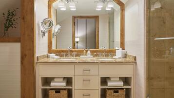 Un baño con un espejo grande, dos lavamanos y una ducha. Hay toallas y cestas en el mueble del lavabo.