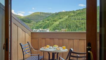 A balcony with a table set for breakfast, overlooking a mountainous landscape.