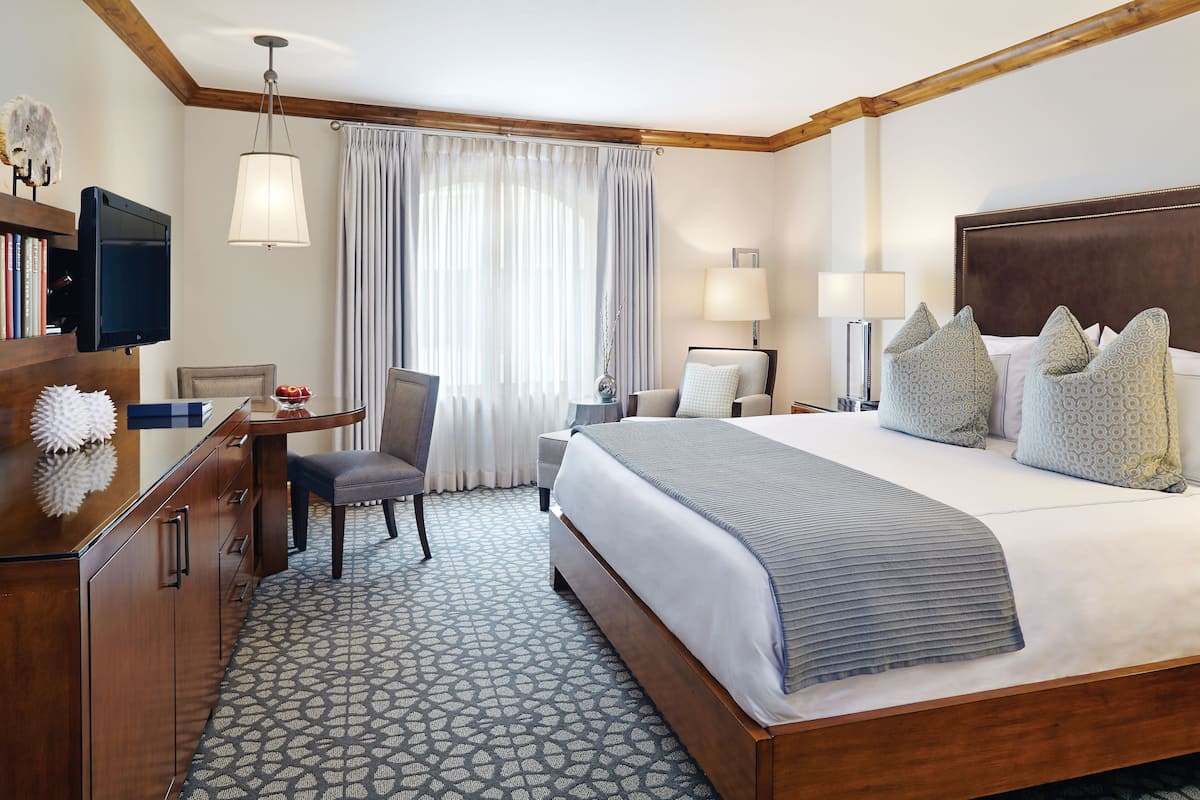 A hotel room with a large bed, a desk with a chair, a TV, and a window with curtains.