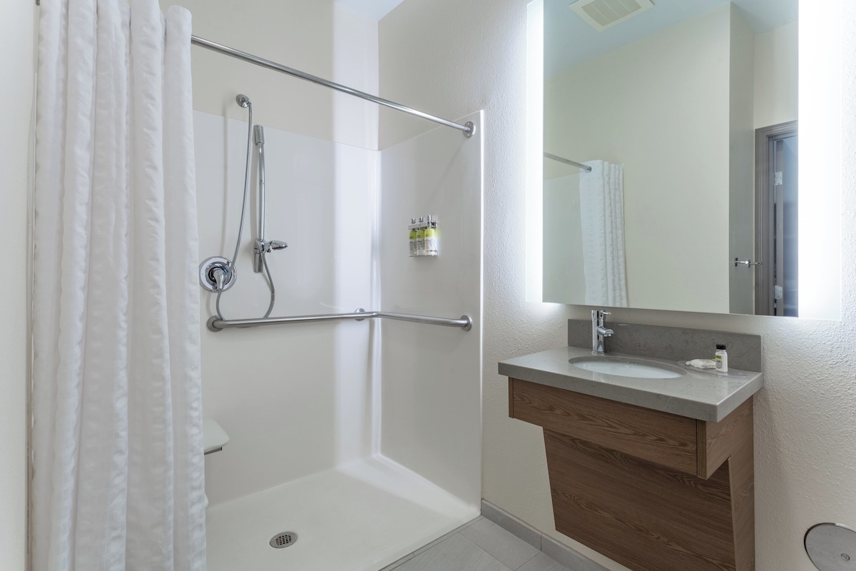 A bathroom with a shower, a grab bar, a sink, and a mirror.
