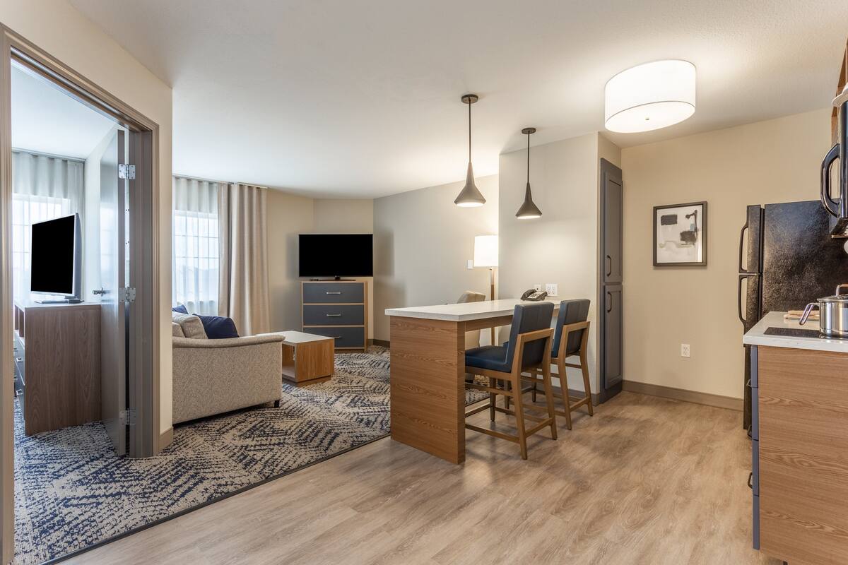 A modern hotel room with a living area, a dining space, and a kitchenette.