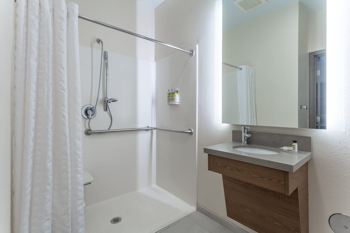 A bathroom with a shower, a grab bar, a sink, and a mirror.