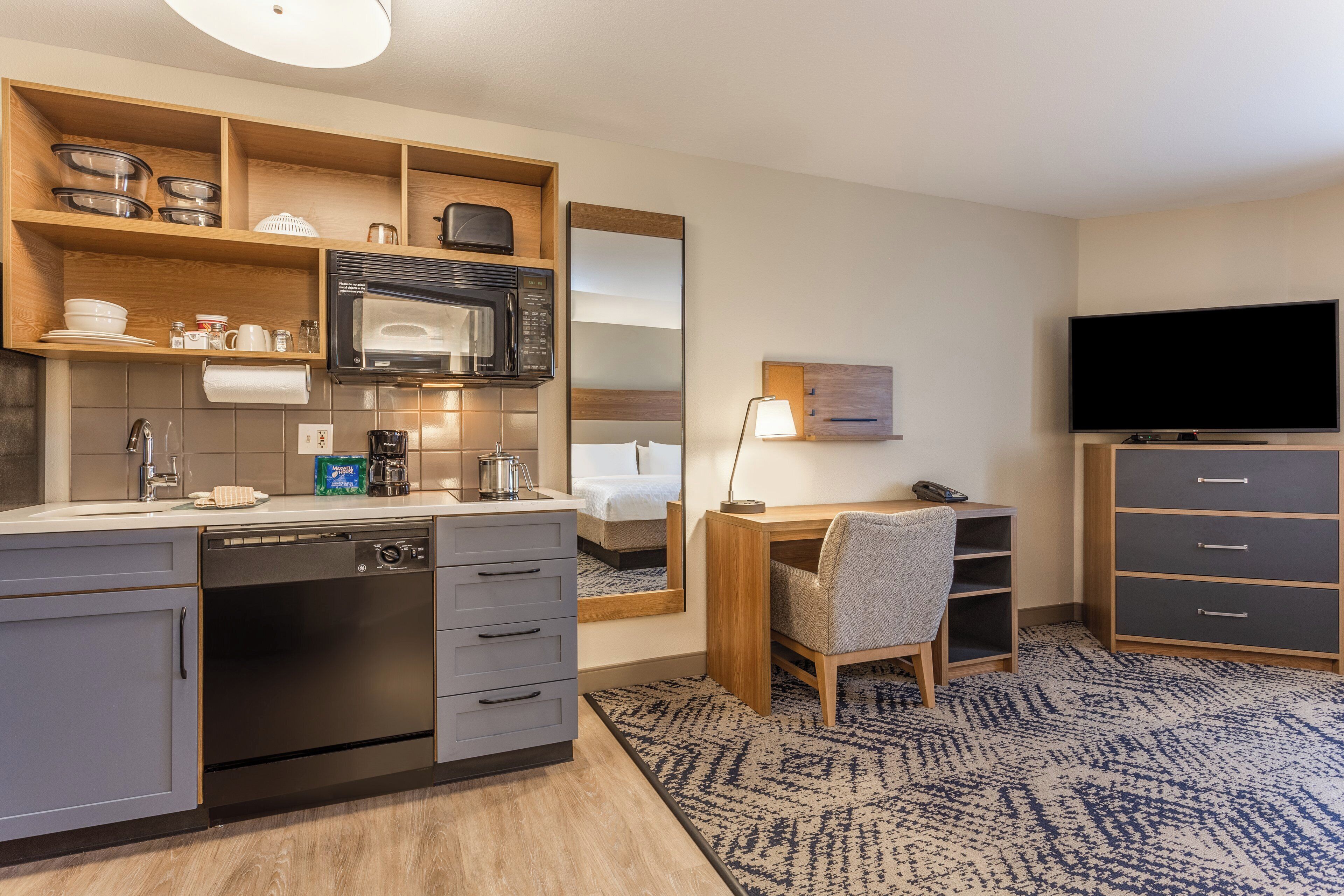 Habitación de hotel compacta con kitchenette, una cama, un escritorio con silla, un televisor y un mueble pequeño.