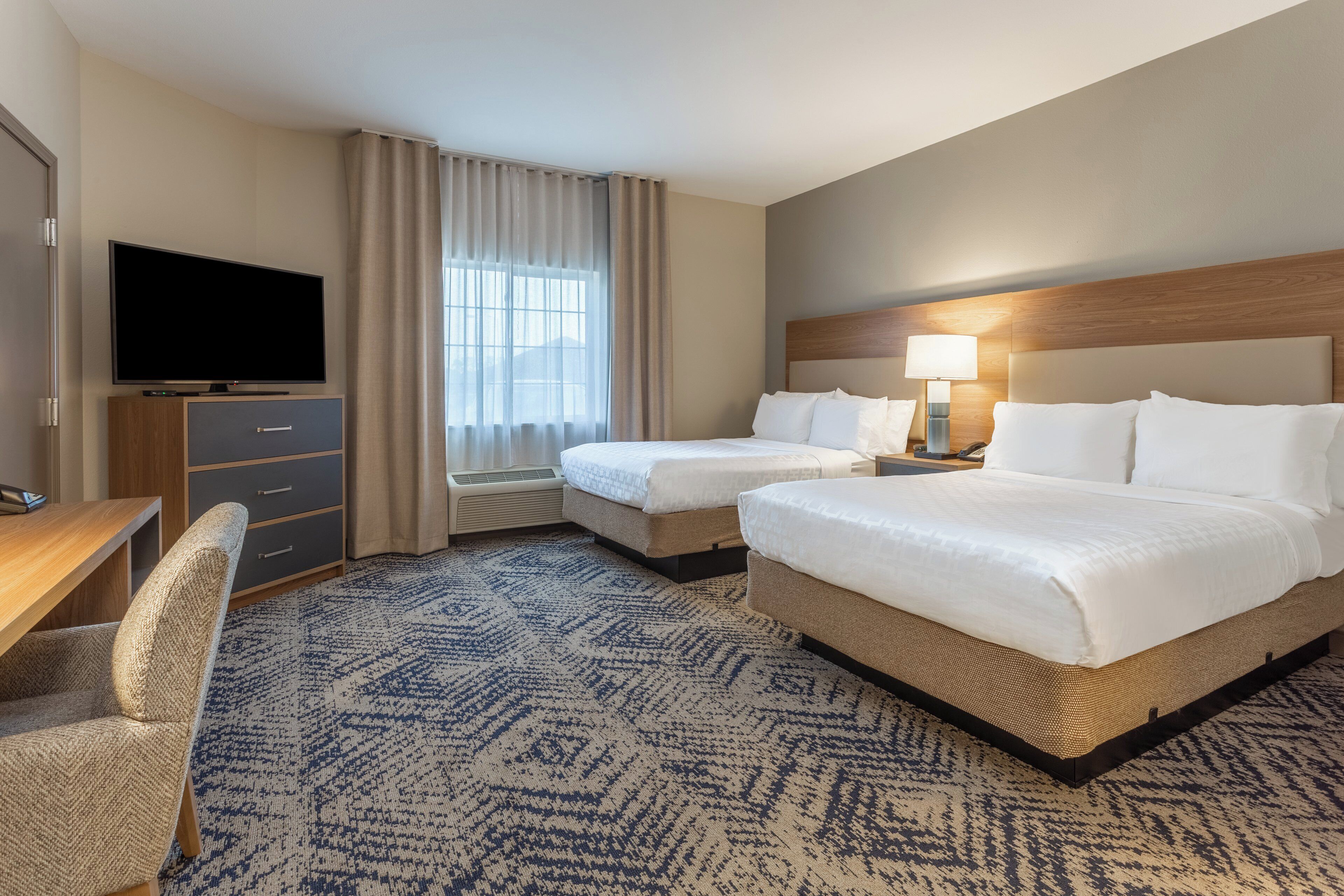 A hotel room with two beds, a TV, a desk, and a chair.