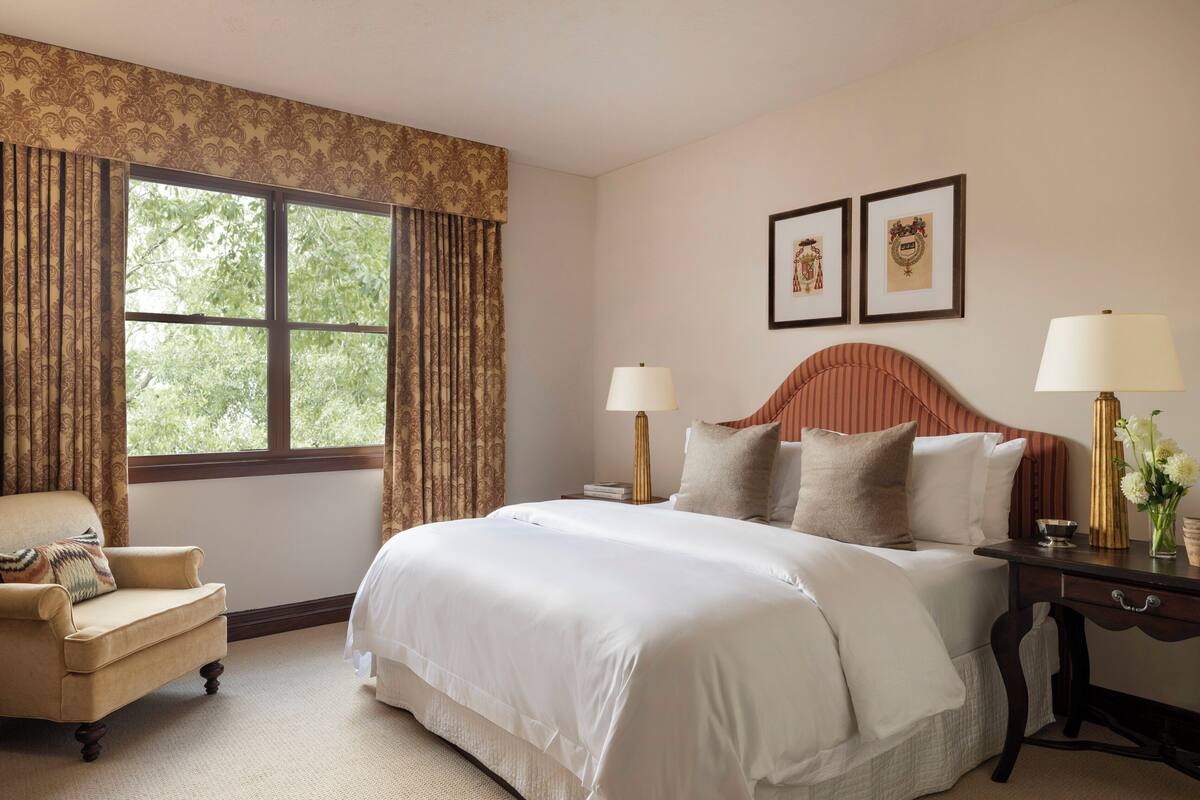 A bedroom with a large bed, two bedside tables, a chair, and a window with curtains.