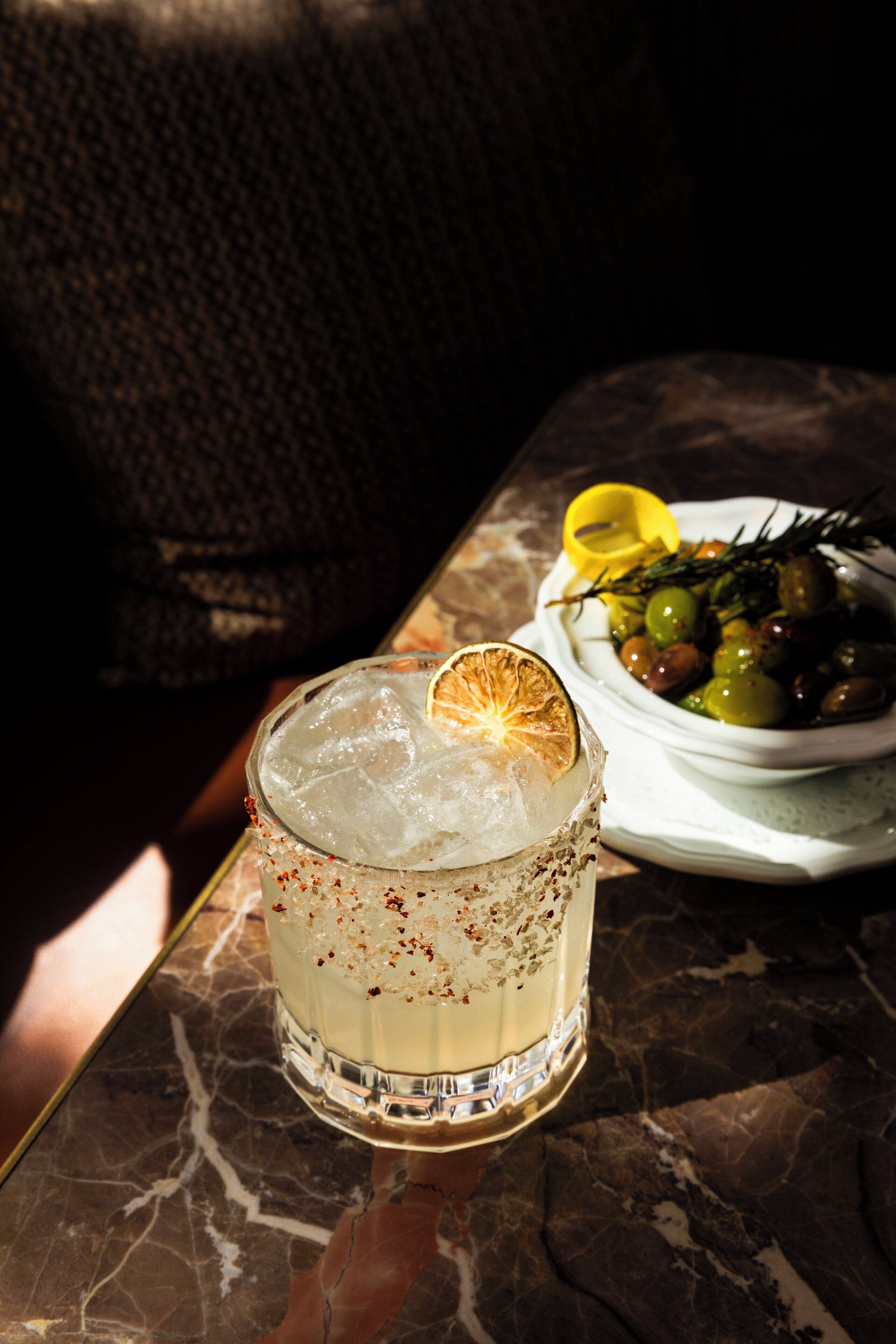 Un verre de cocktail avec des glaçons et une tranche d’orange, posé sur une table en marbre.