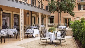 An outdoor dining area with tables and chairs, a covered section with windows, and a tree.