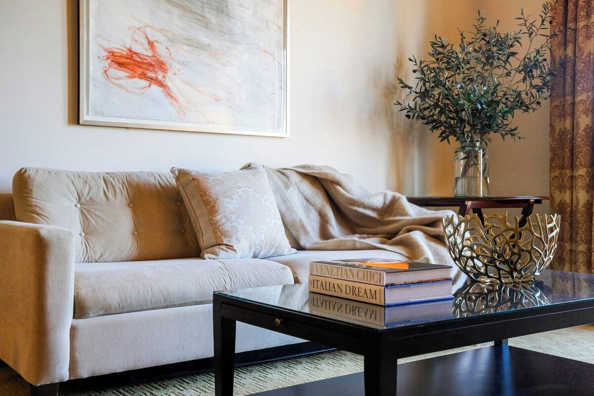 A living room with a sofa, a coffee table, a vase with plants, and a framed abstract painting.