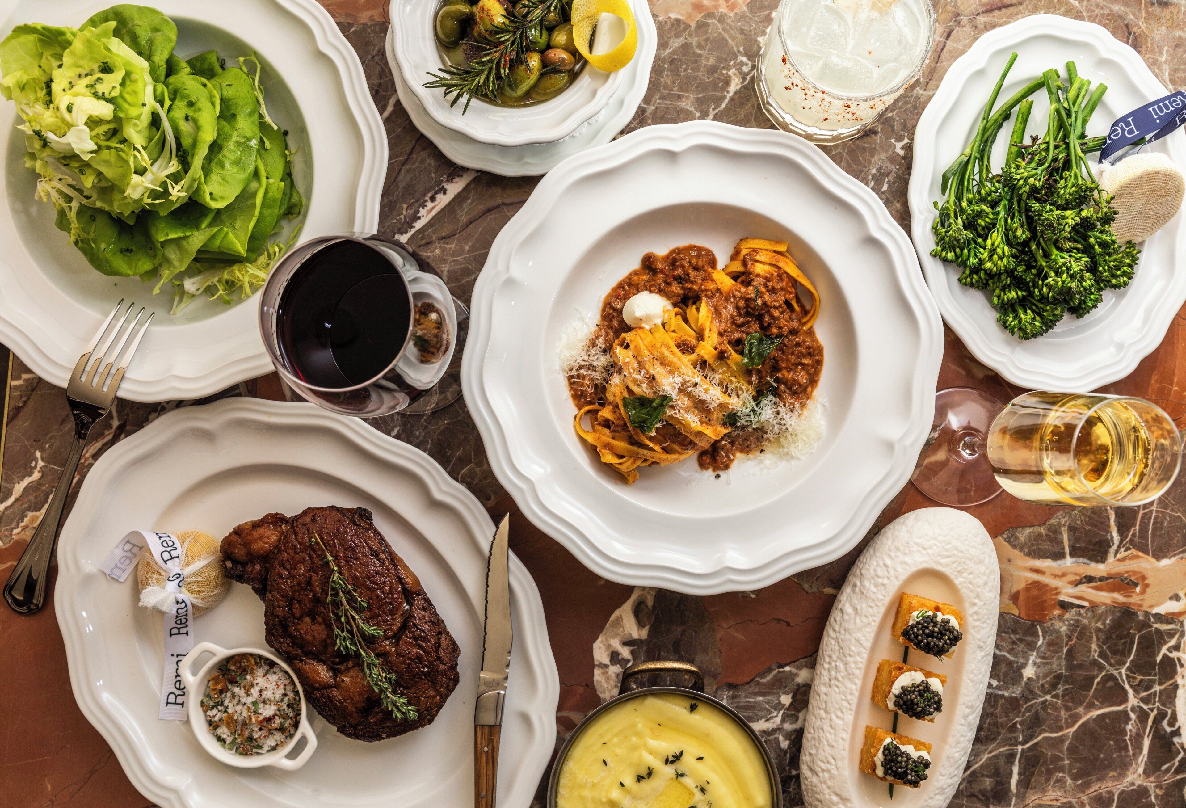Une table garnie de divers plats, notamment des pâtes, de la viande et des légumes, ainsi que des boissons et des condiments.