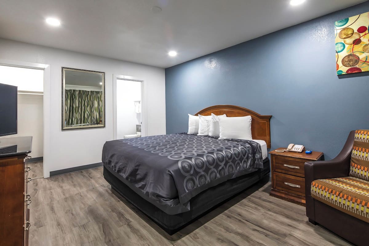 A hotel room with a large bed, a wooden nightstand, a desk with a computer, and a chair.