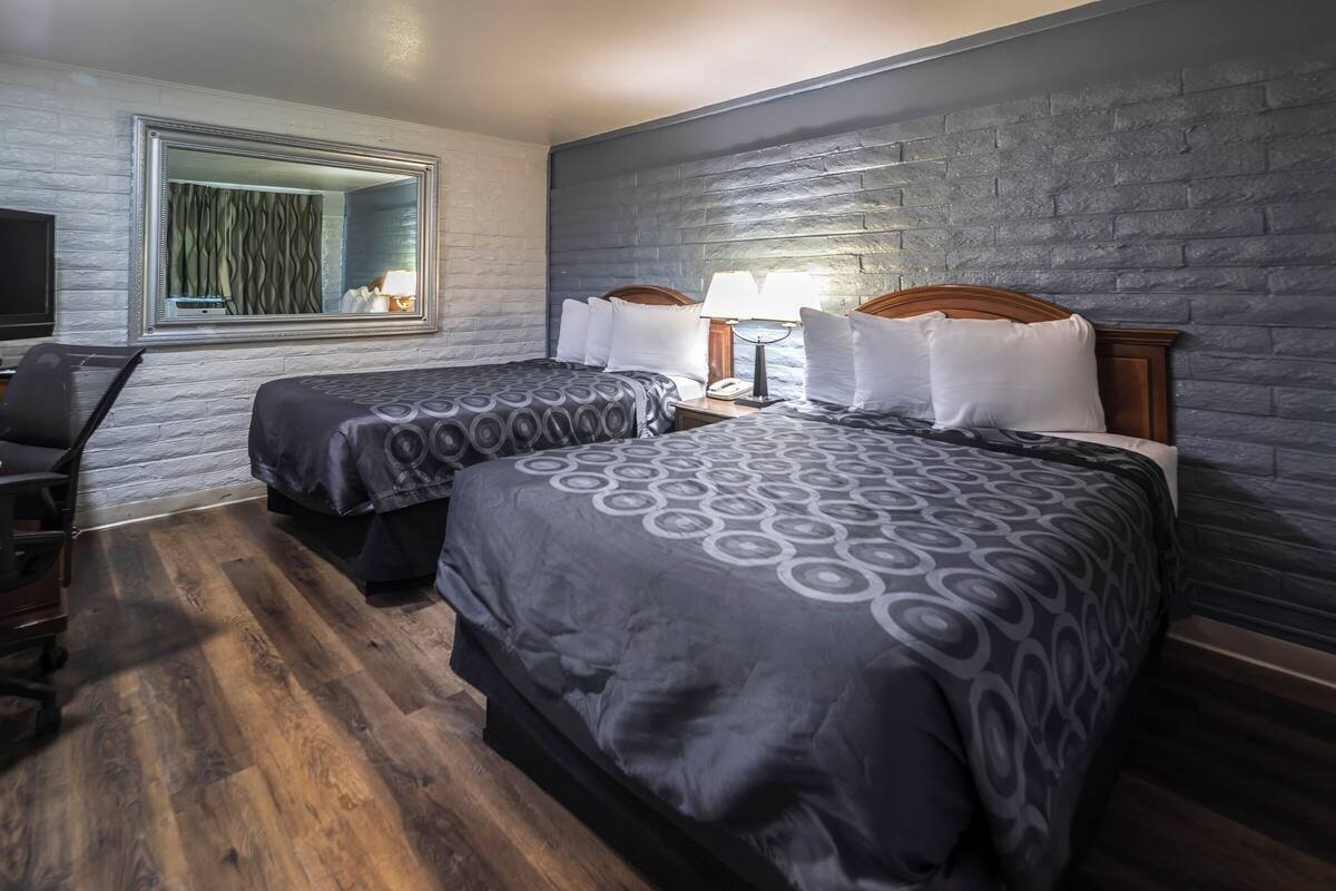 A hotel room with two beds, a desk, and a television.