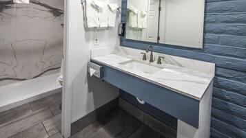 A bathroom with a marble-tiled wall, a white bathtub, a sink with a blue countertop, and a mirror above the sink.