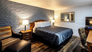A hotel room with a bed, a desk, a chair, a nightstand, and a lamp. - Hitching Post Studios Inn (Santa Cruz)