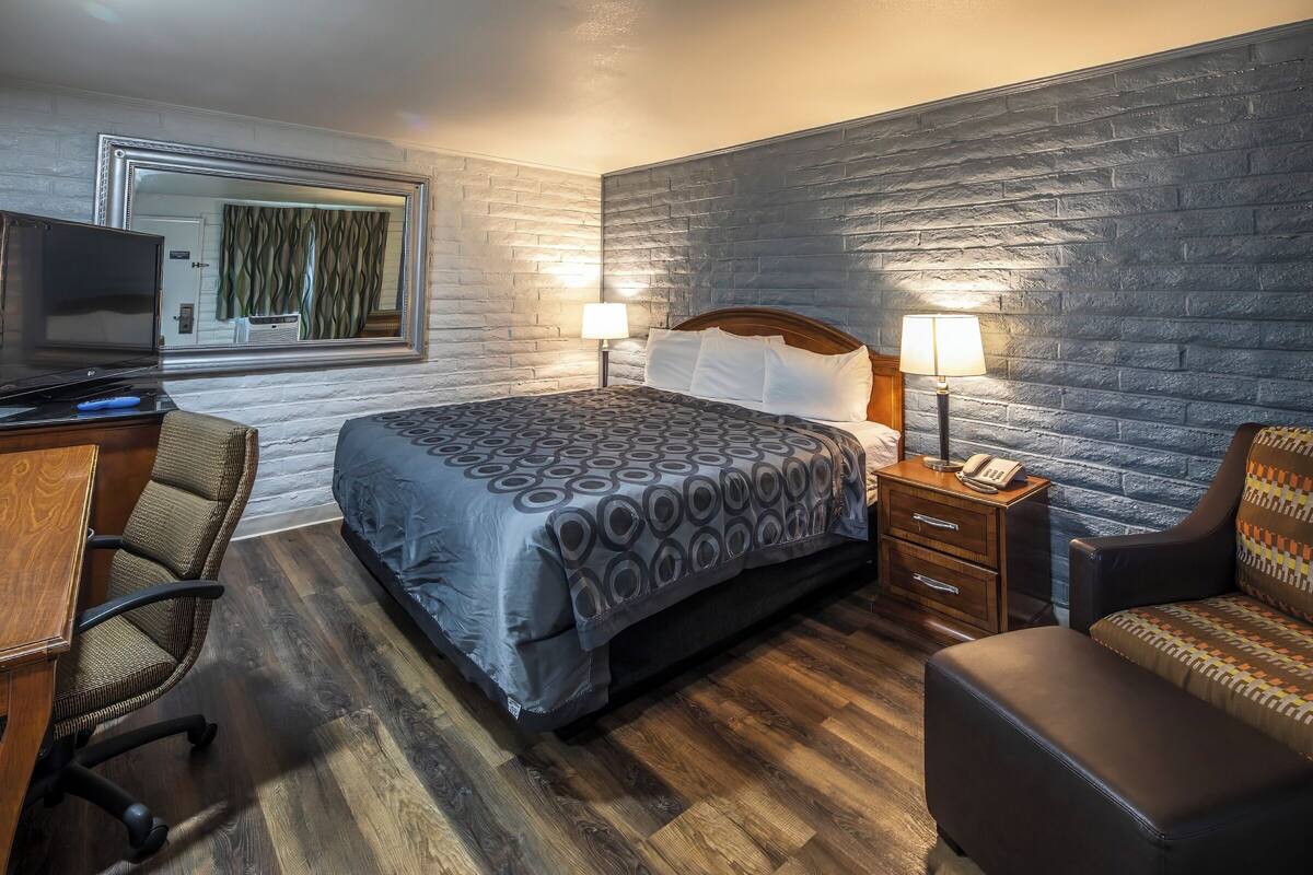 A hotel room with a bed, a desk with a computer, a chair, a sofa, and a TV.