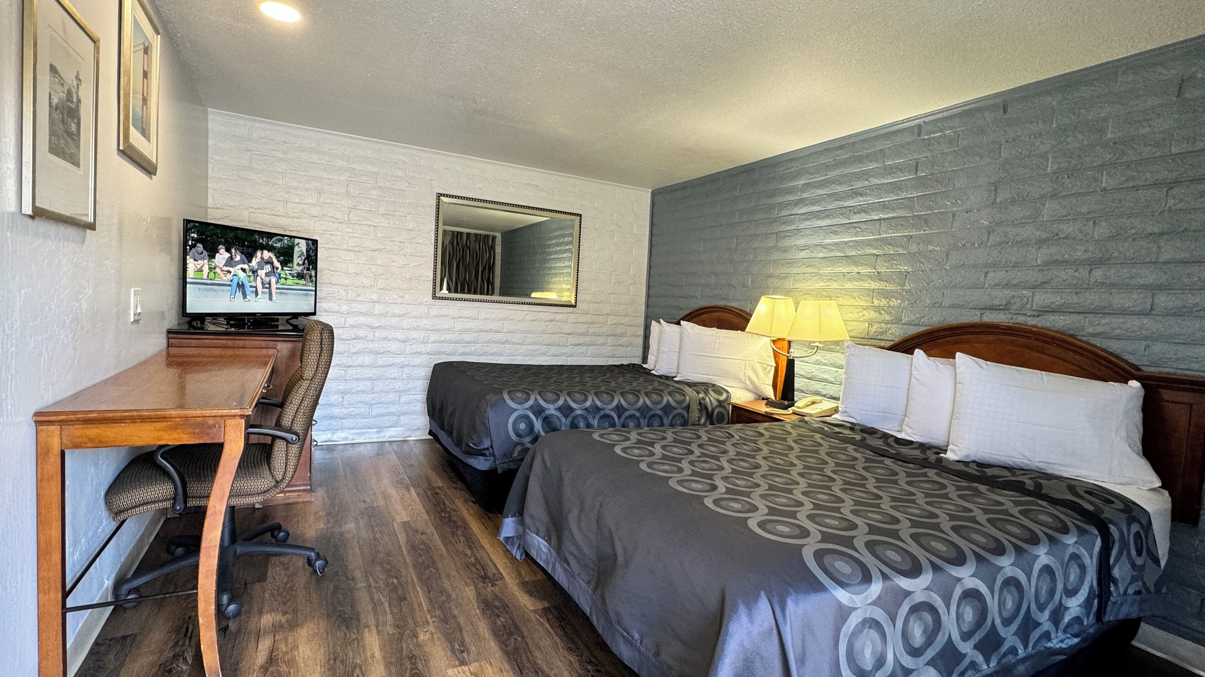 A hotel room with two beds, a desk with a chair, a television, and a mirror.