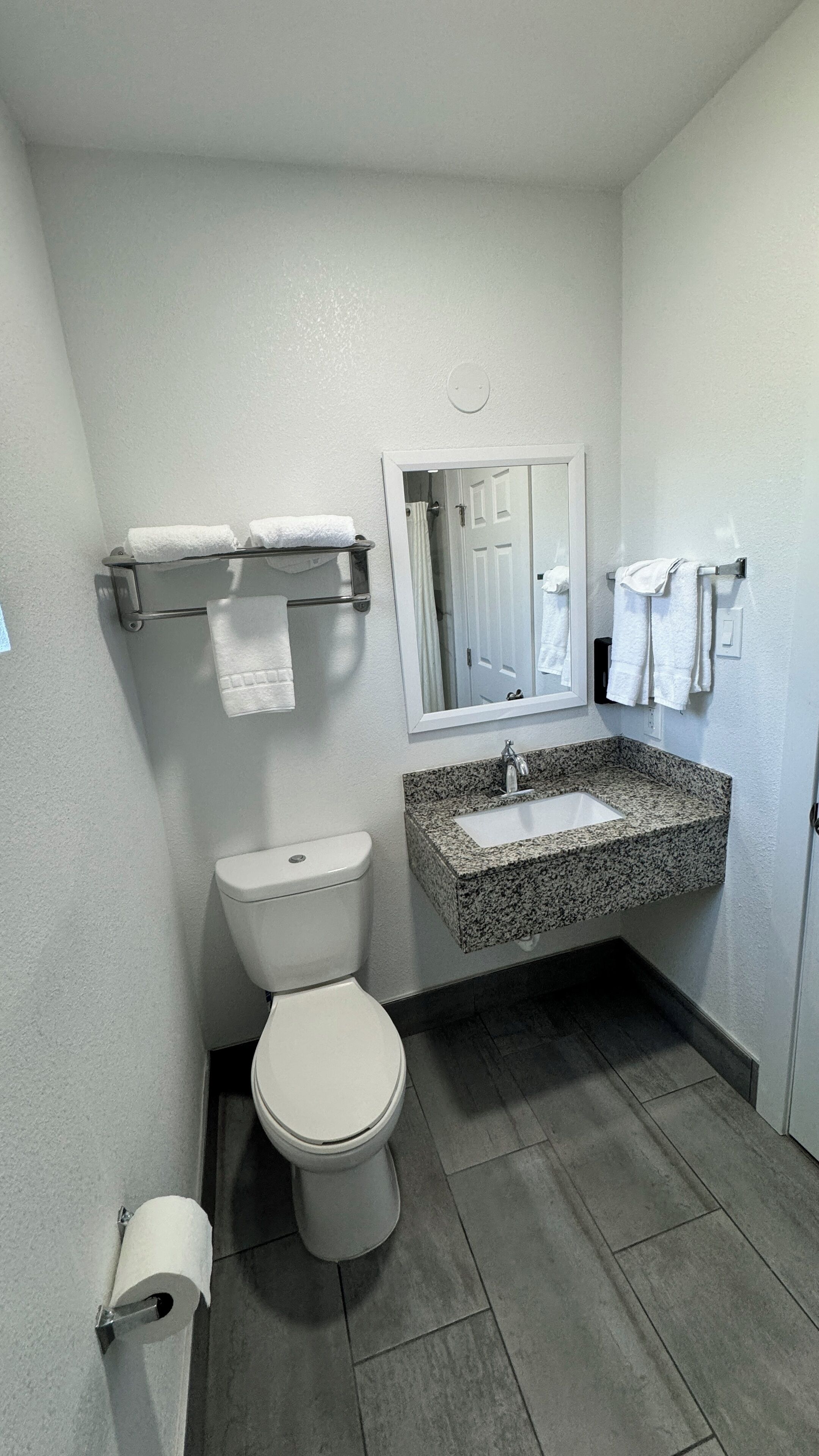 A compact bathroom with a toilet, a granite sink, and a mirror above the sink.