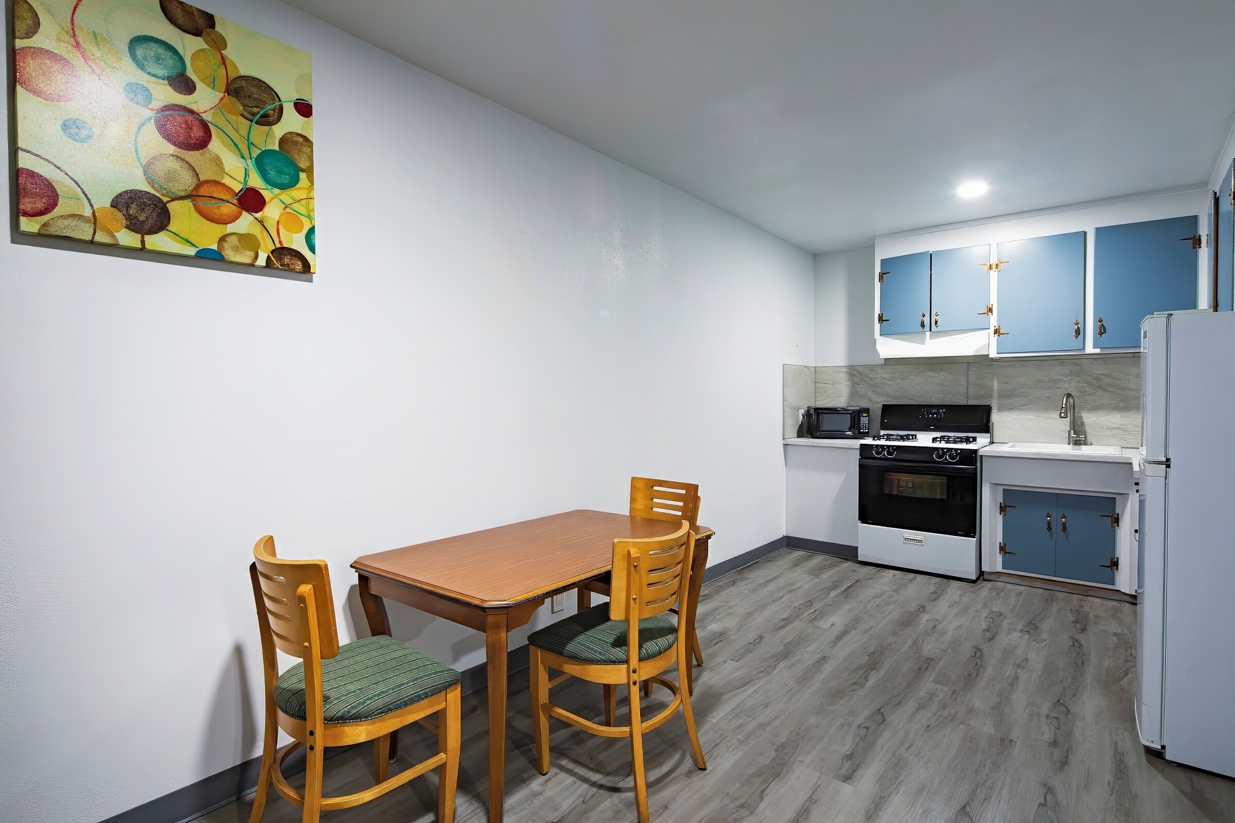 Une cuisine compacte avec des meubles en bois, une table à manger avec des chaises et un tableau abstrait aux couleurs vives accroché au mur.