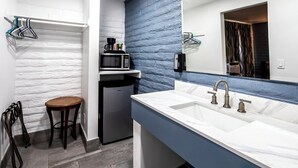 A compact bathroom with a white sink, a mirror, a microwave, and a small refrigerator. - Hitching Post Studios Inn (Santa Cruz)