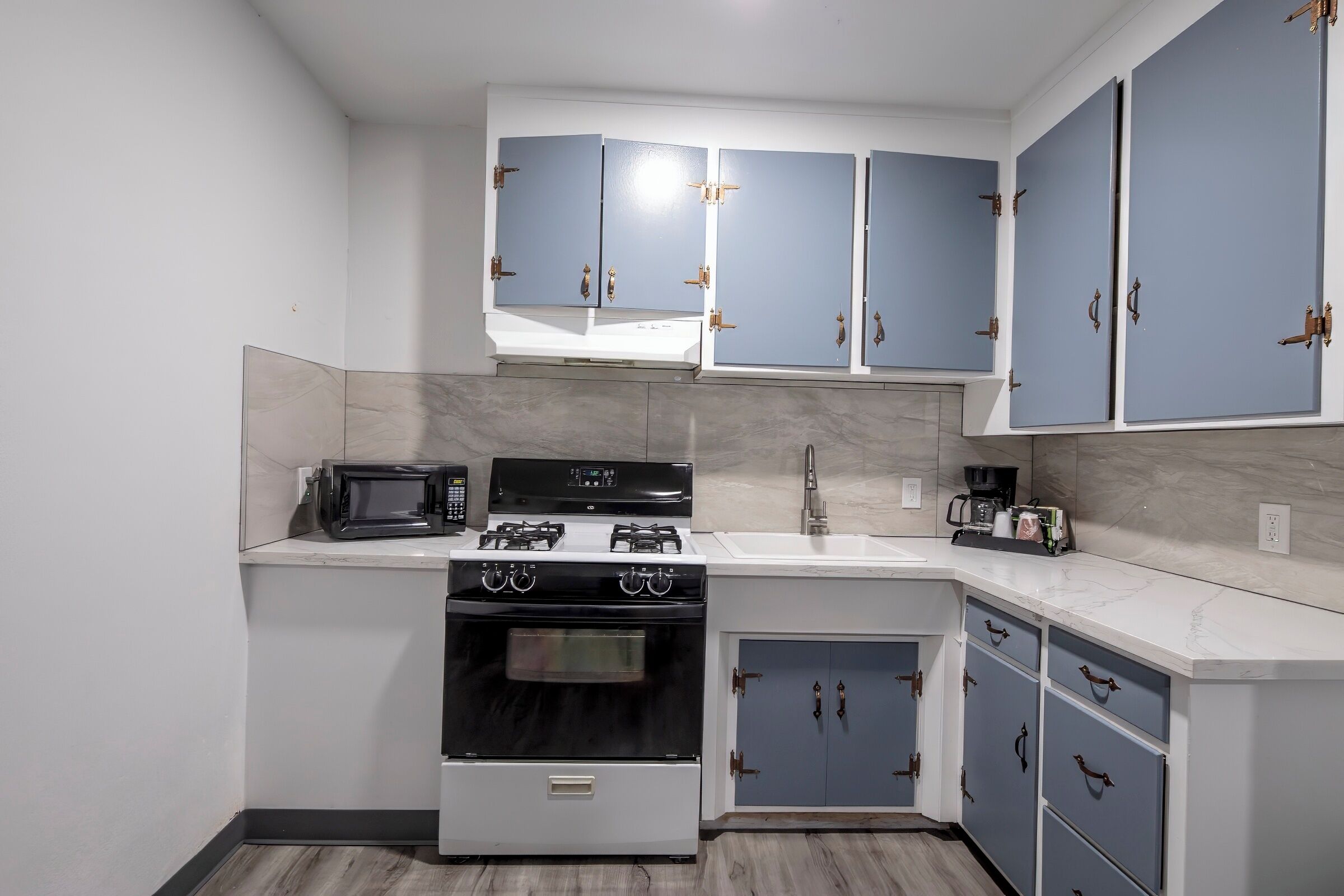 A compact kitchen with white cabinets, a microwave, a stove, and a coffee maker.