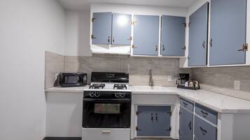 A compact kitchen with white cabinets, a microwave, a stove, and a coffee maker.