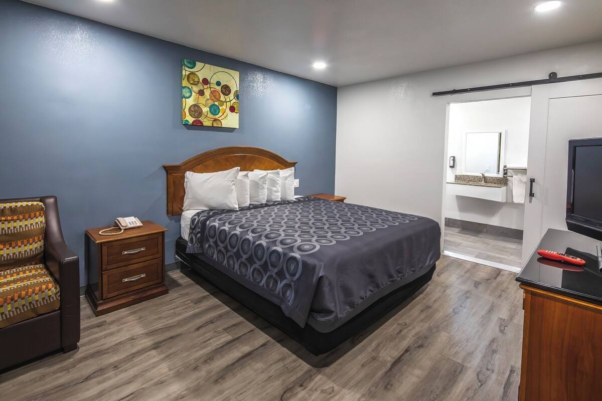 A bedroom with a bed, a nightstand, a chair, a desk, and a TV.