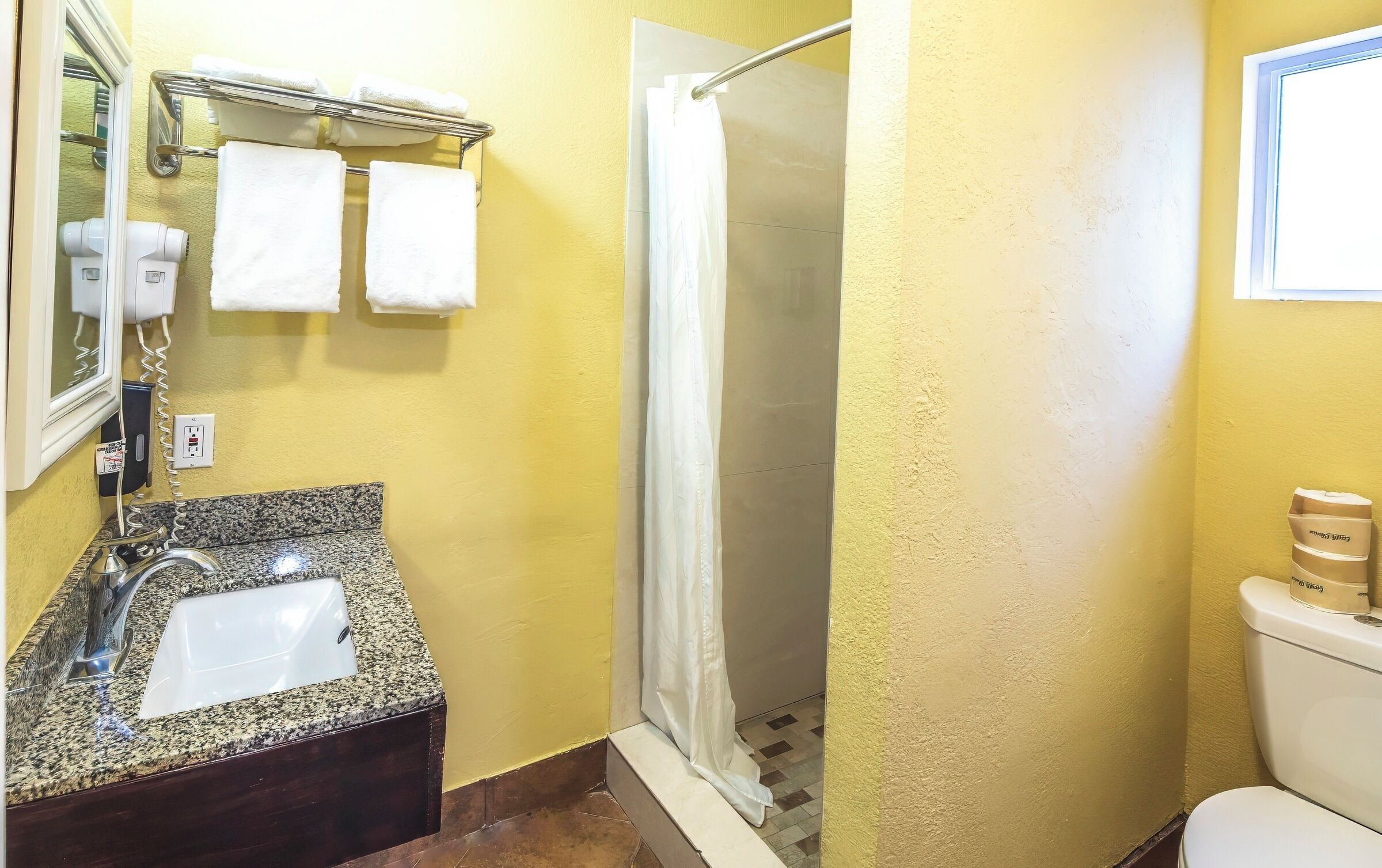 A bathroom with a granite sink, white towels, a shower curtain, and a toilet.