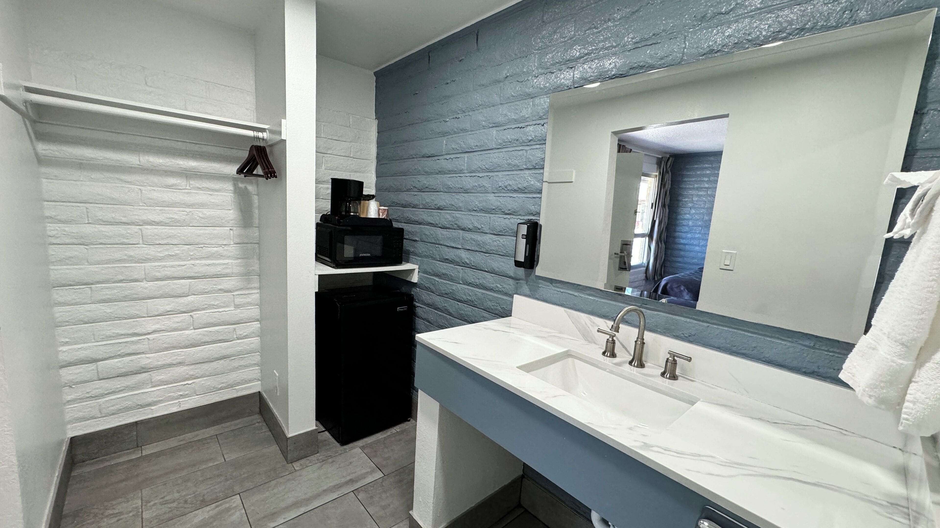 A bathroom with a white sink, a black refrigerator, a towel rack, and a blue brick wall.