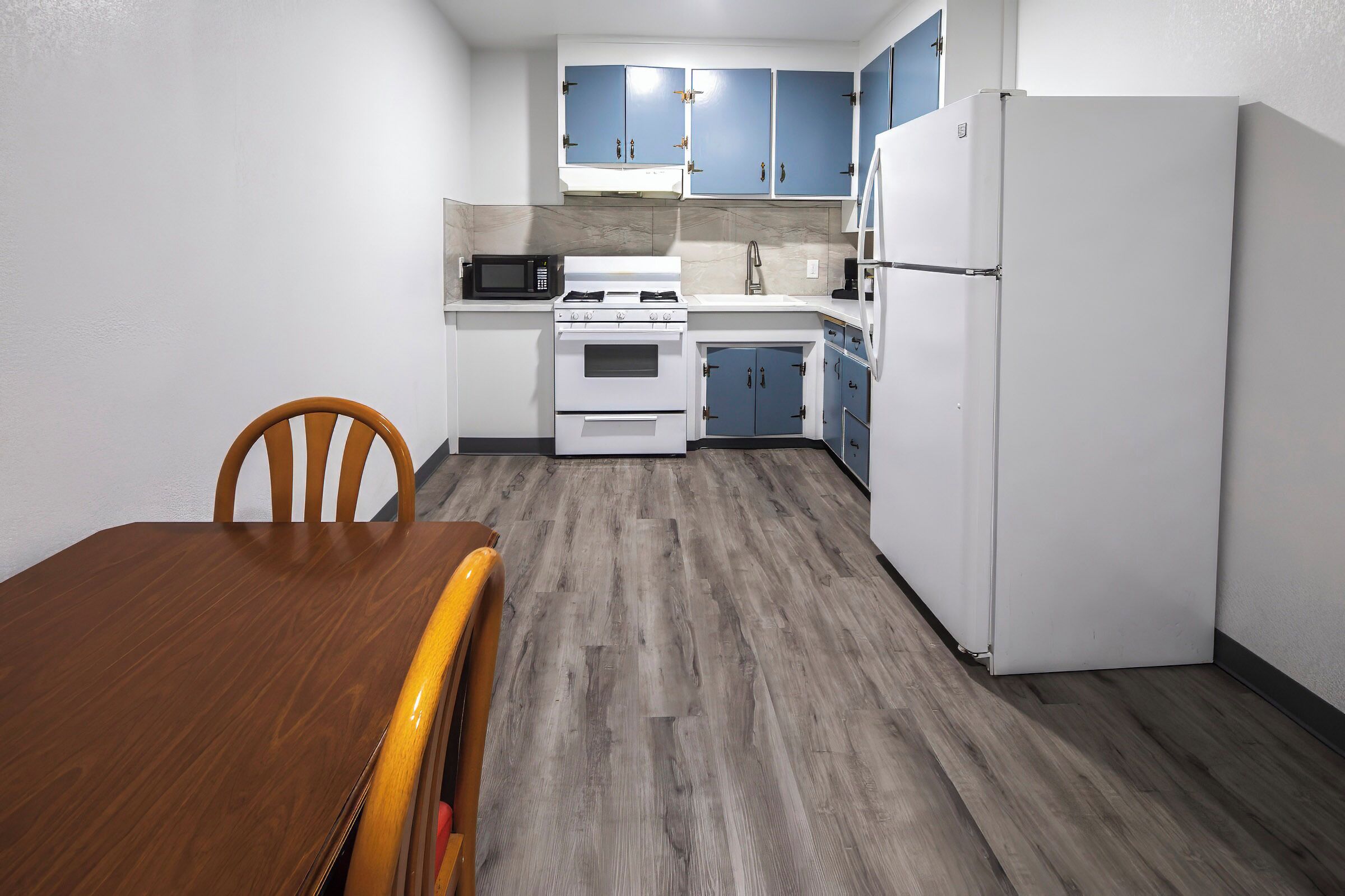 A compact kitchen with white appliances, blue cabinets, and a wooden dining table.