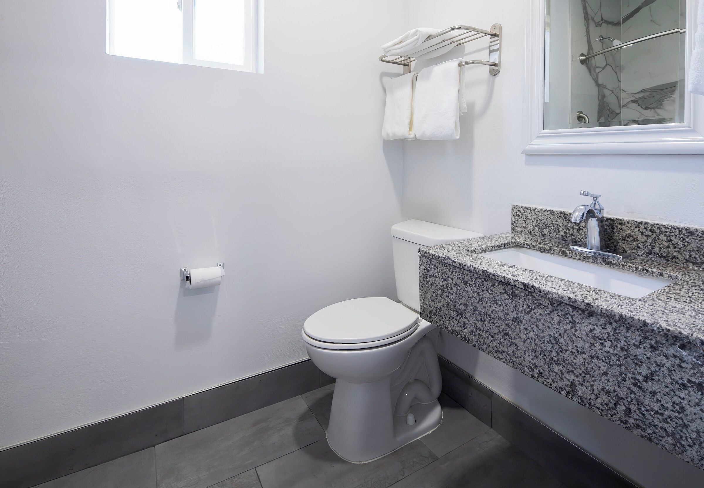 A modern bathroom with a white toilet, granite countertop sink, and a towel rack with two towels.