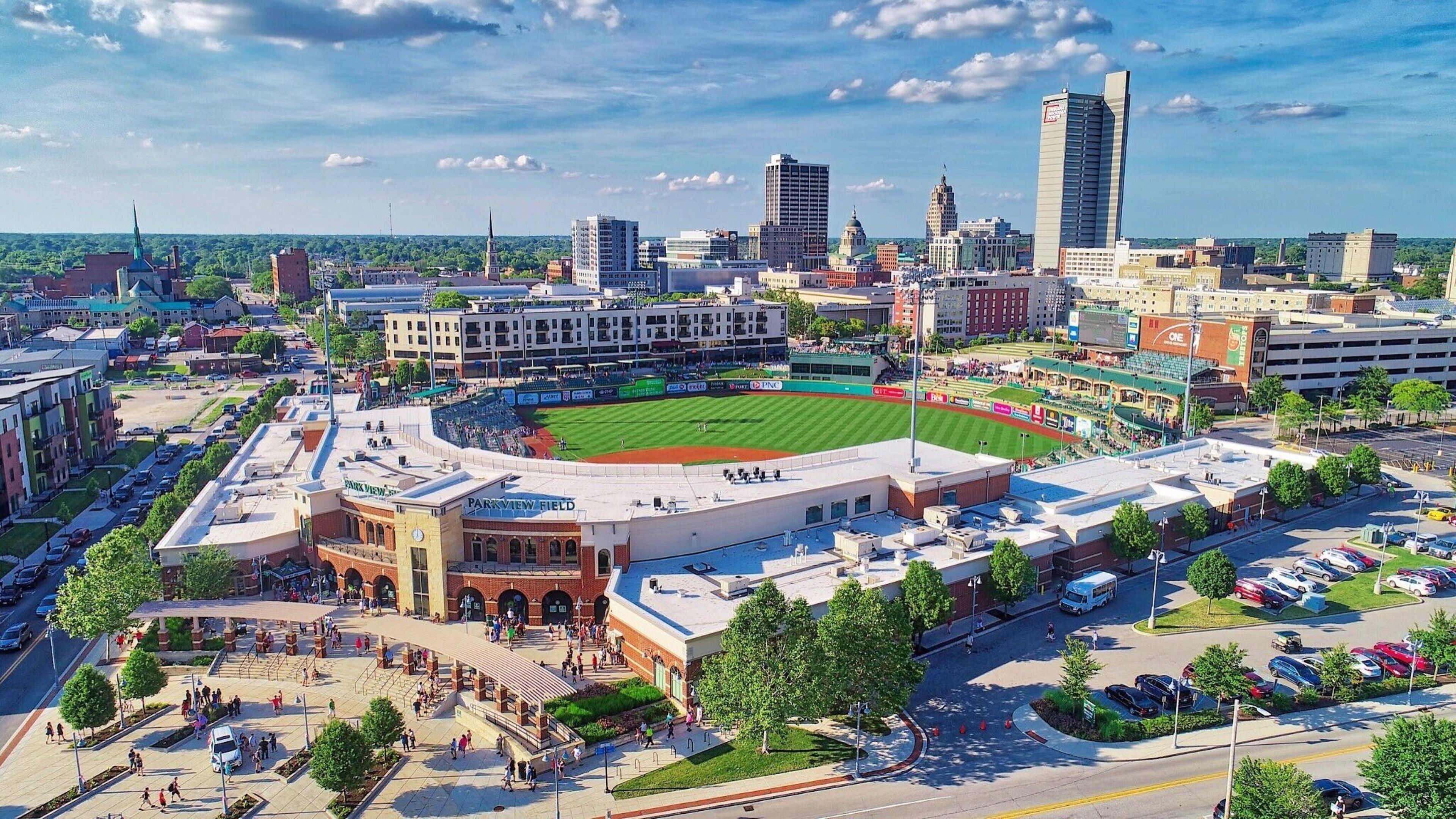 A stadium with a baseball field surrounded by parking and commercial buildings.