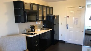A compact kitchen with black cabinets, a microwave, a refrigerator, and a coffee maker. - Candlewood Suites Fort Wayne by IHG (Fort Wayne)