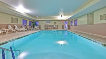 Una piscina interior con agua cristalina, líneas de profundidad marcadas y una silla para socorrista.
