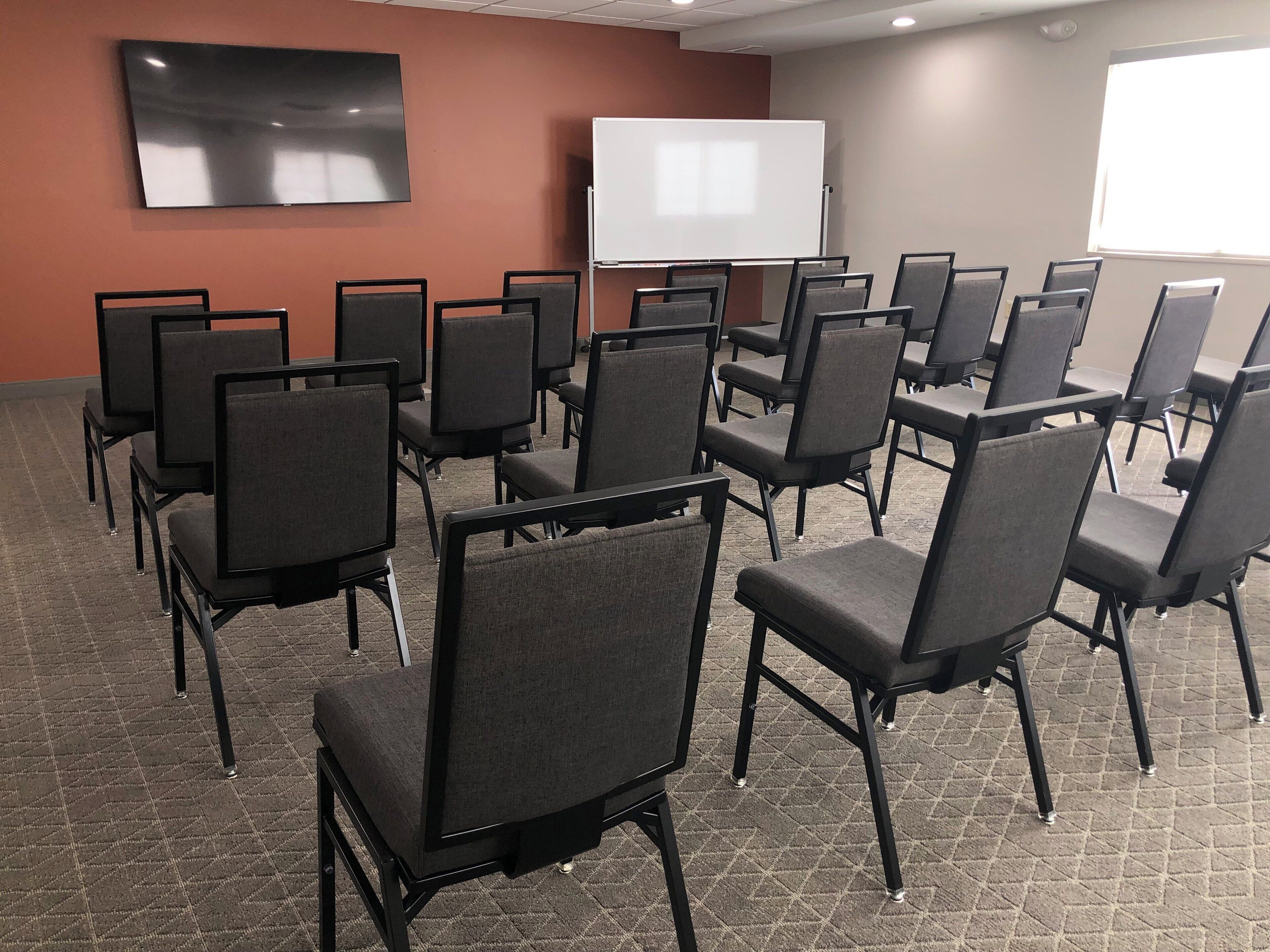 A conference room with rows of chairs, a whiteboard, and a flat-screen TV on the wall.