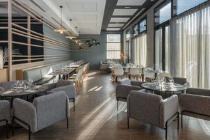 Un restaurante moderno con mesas largas, sillas tapizadas en gris y amplios ventanales que dejan entrar luz natural.