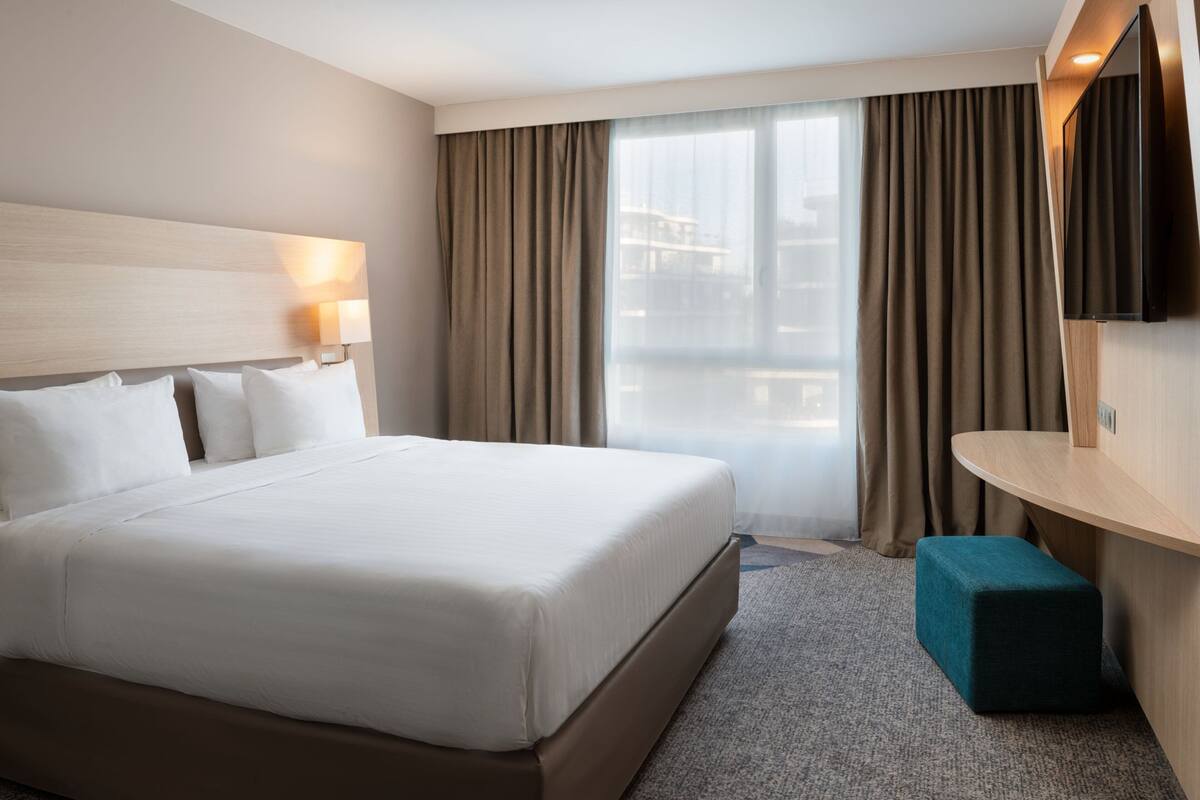 Een hotelkamer met een groot bed, een bureau met een flatscreen televisie en uitzicht op de stad.