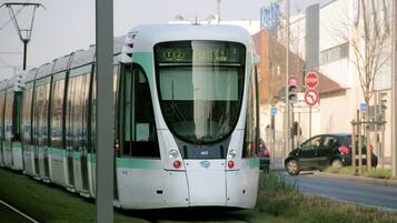 A modern tram with a digital display, moving along a track beside a road with cars and traffic signs.