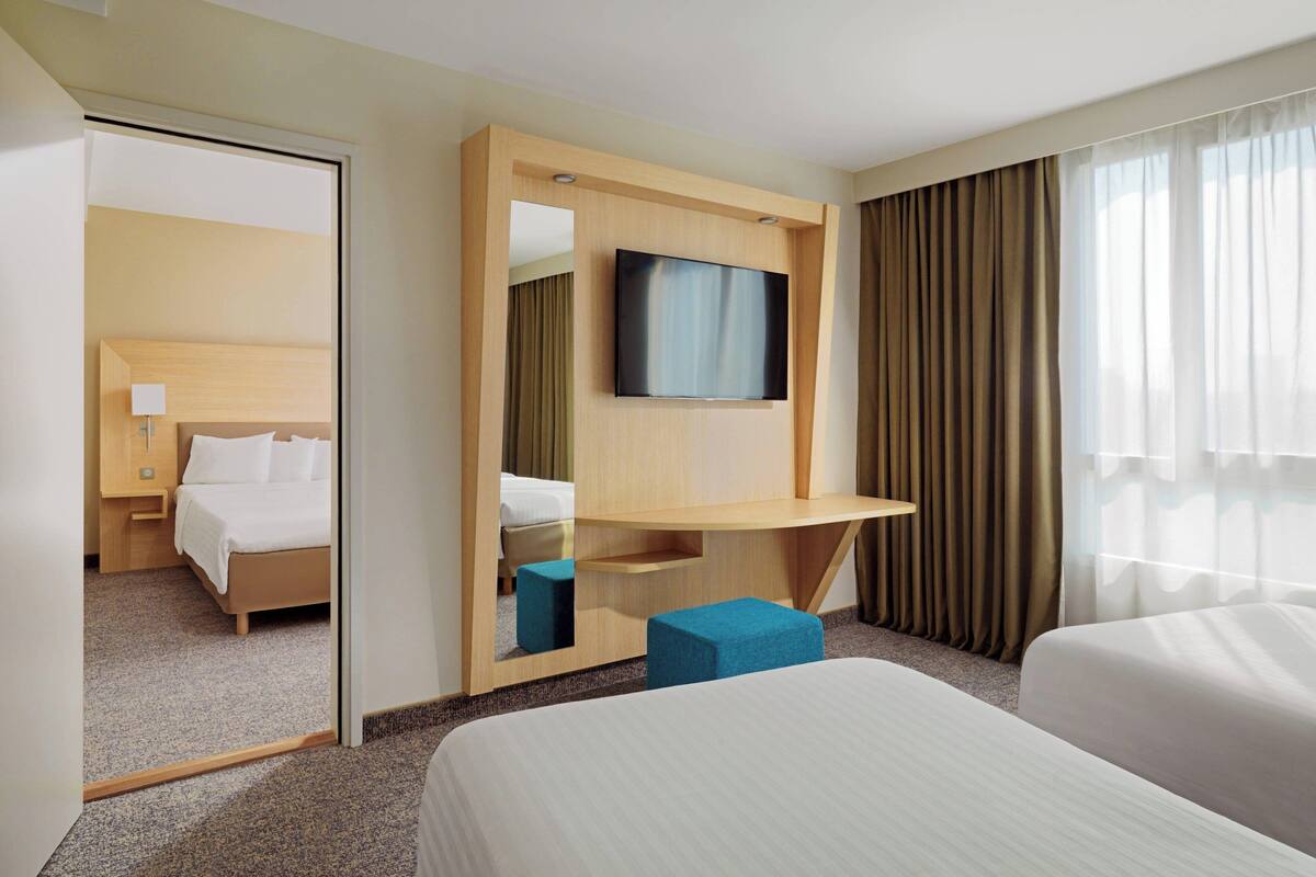 Een hotelkamer met een bed, een bureau met een flatscreen televisie, een spiegel en een raam met gordijnen.
