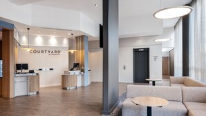 A modern hotel lobby with a reception desk, seating area, and a sign for the Courtyard by Marriott.
