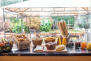 Un bufé de desayuno con pan, bollería, frutas y bebidas sobre una mesa bajo una marquesina.