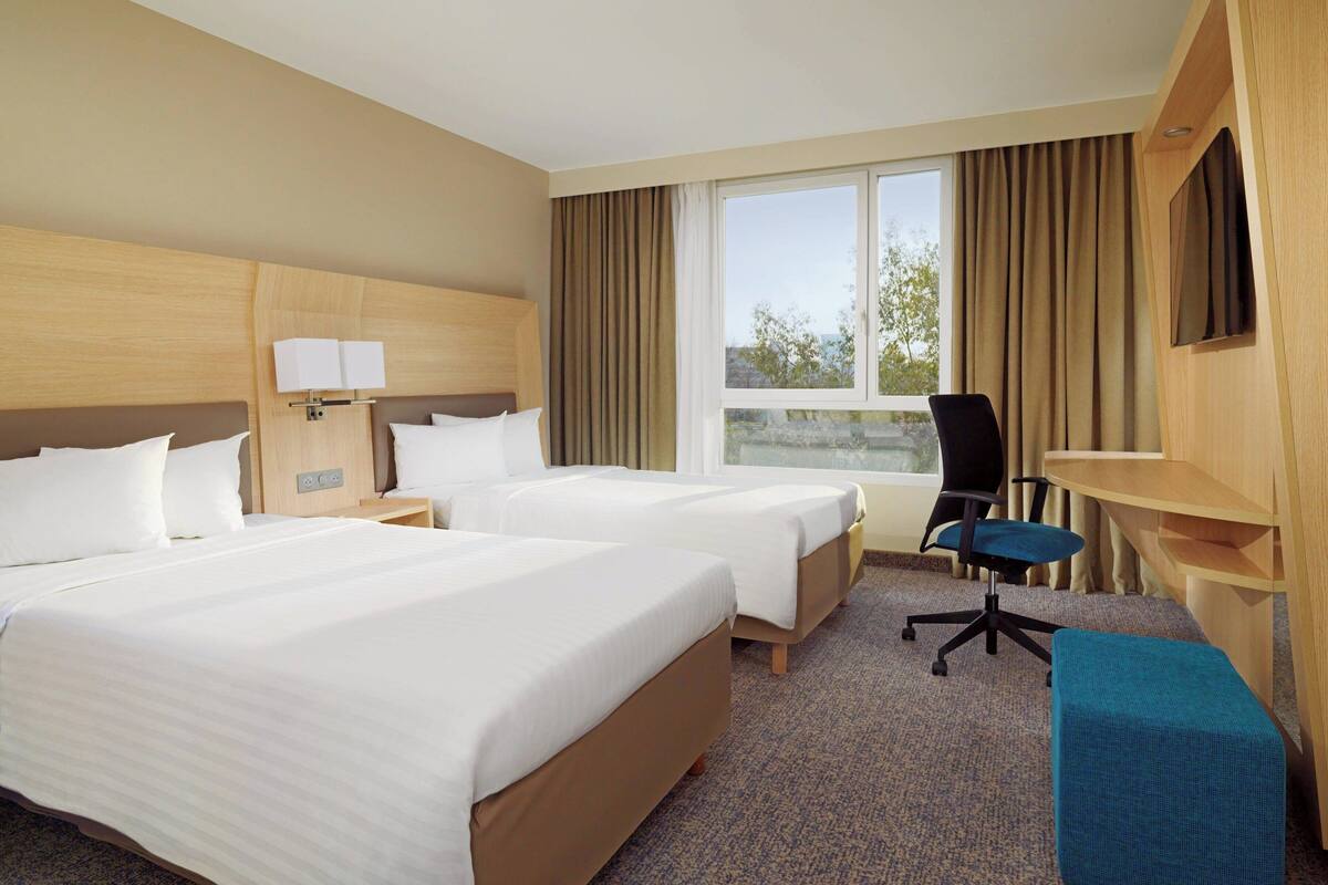 Een hotelkamer met twee bedden, een bureau, een stoel en een groot raam met gordijnen.