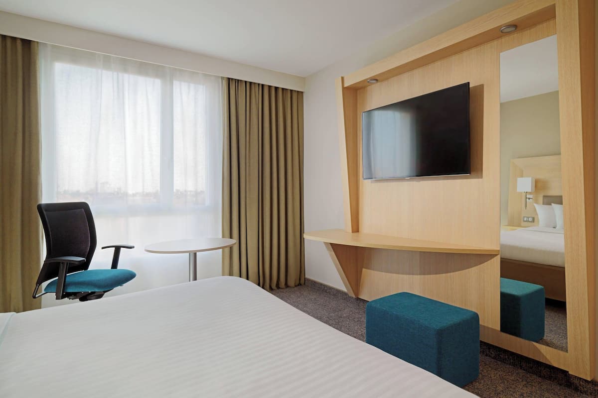Een hotelkamer met een groot bed, een bureau, een stoel, een televisie en een spiegel.
