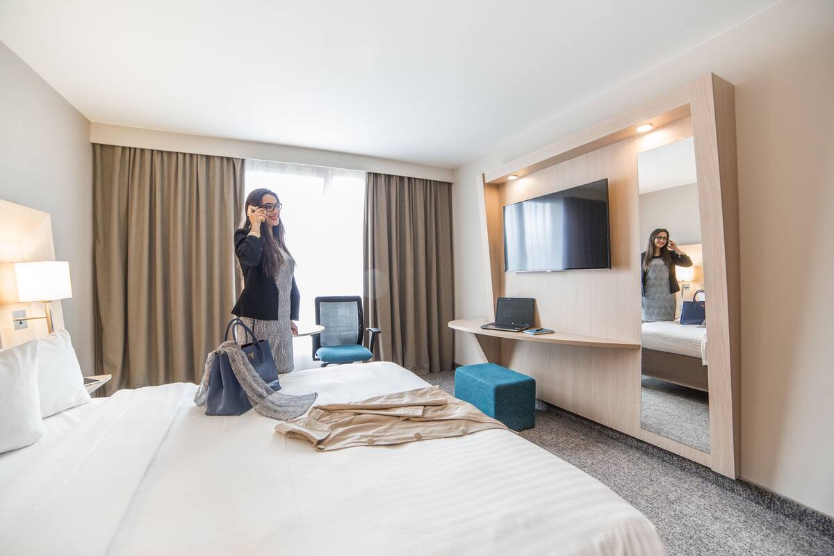 Een hotelkamer met een bed, een bureau, een stoel, een televisie en een groot raam met gordijnen.
