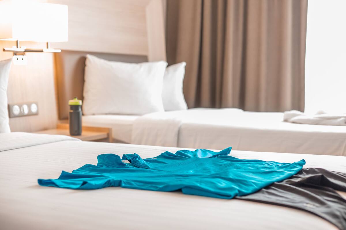 Een hotelkamer met een opgemaakt bed, een nachtkastje met een lamp en een raam met gordijnen.