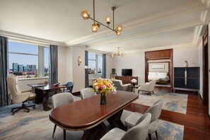 Une chambre d’hôtel spacieuse avec une grande table à manger, des sièges confortables, une vue sur la ville et un lustre moderne.