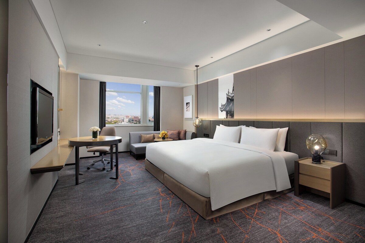 Une chambre d’hôtel avec un grand lit, un bureau, une chaise, une télévision et une fenêtre donnant sur la ville.