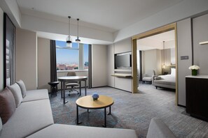 Une chambre d’hôtel moderne avec un canapé, une petite table ronde, un téléviseur et une vue sur la ville.