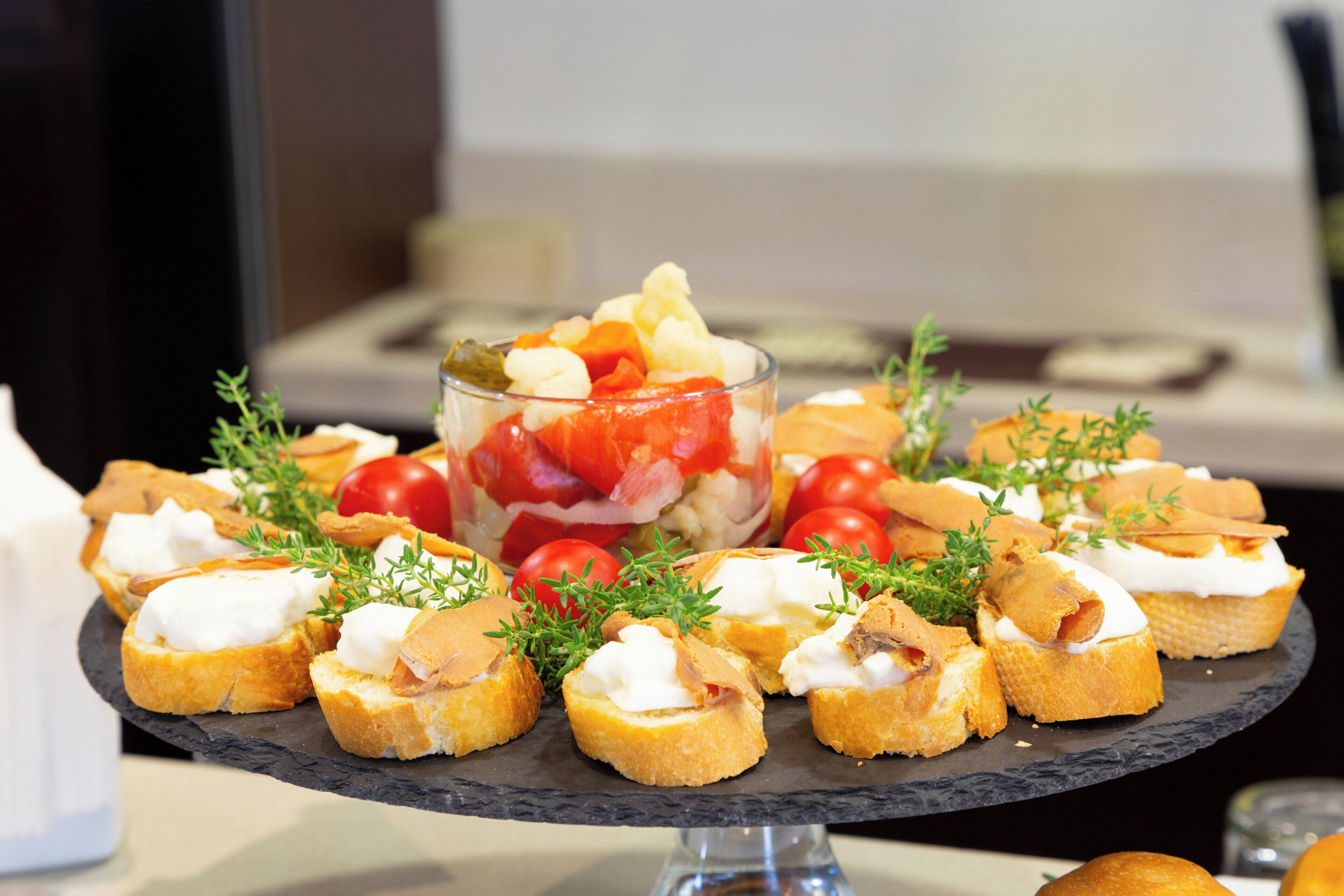 Una bandeja de aperitivos que incluye pan con crema y una ensalada con tomates y otras verduras.